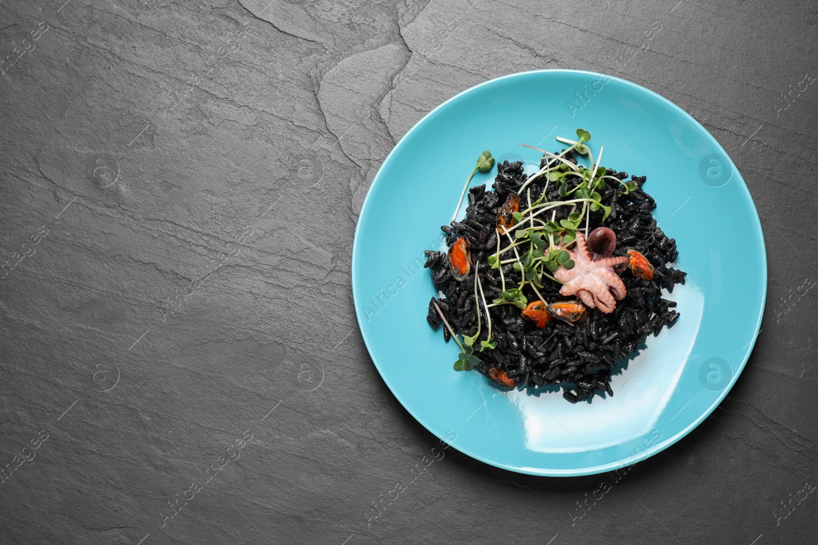 Photo of Delicious black risotto with seafood on grey table, top view. Space for text