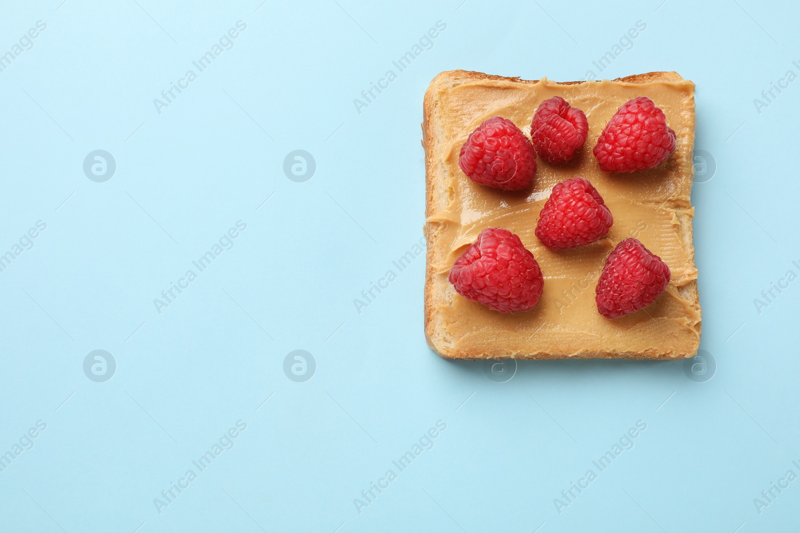 Photo of Tasty peanut butter sandwich with fresh raspberries on light blue background, top view. Space for text