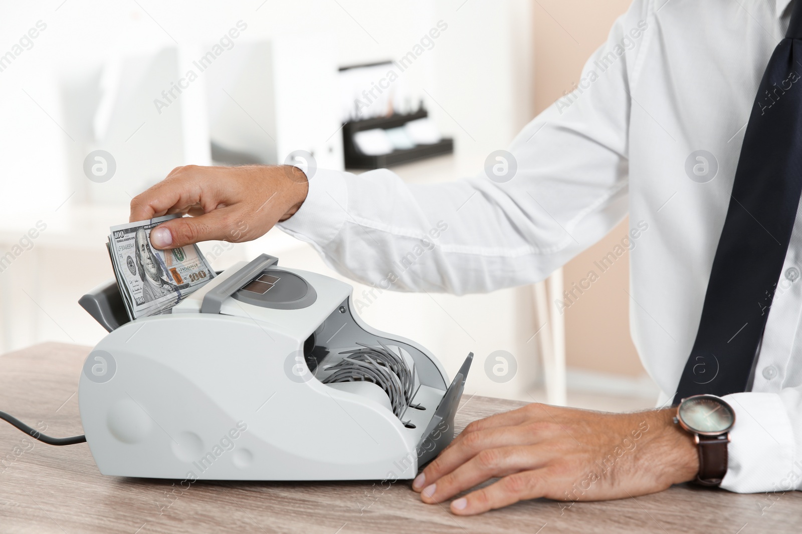 Photo of Male teller putting money into currency counting machine at cash department, closeup