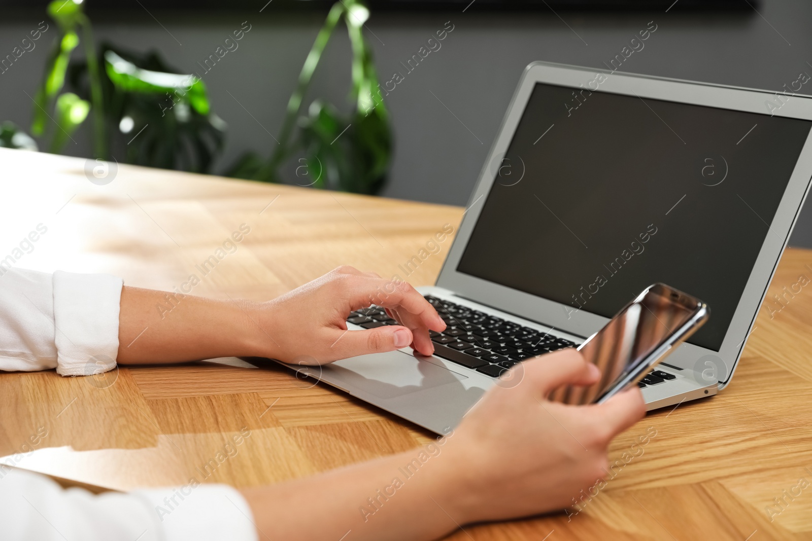 Photo of Woman with modern smartphone and laptop at wooden table indoors, closeup. Searching information