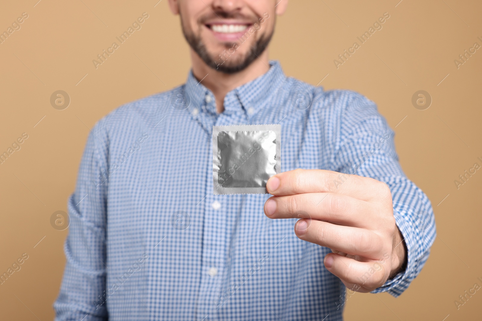 Photo of Happy man holding condom on beige background, closeup