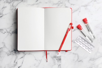 Test tubes, pills and notebook with pen on marble background, flat lay