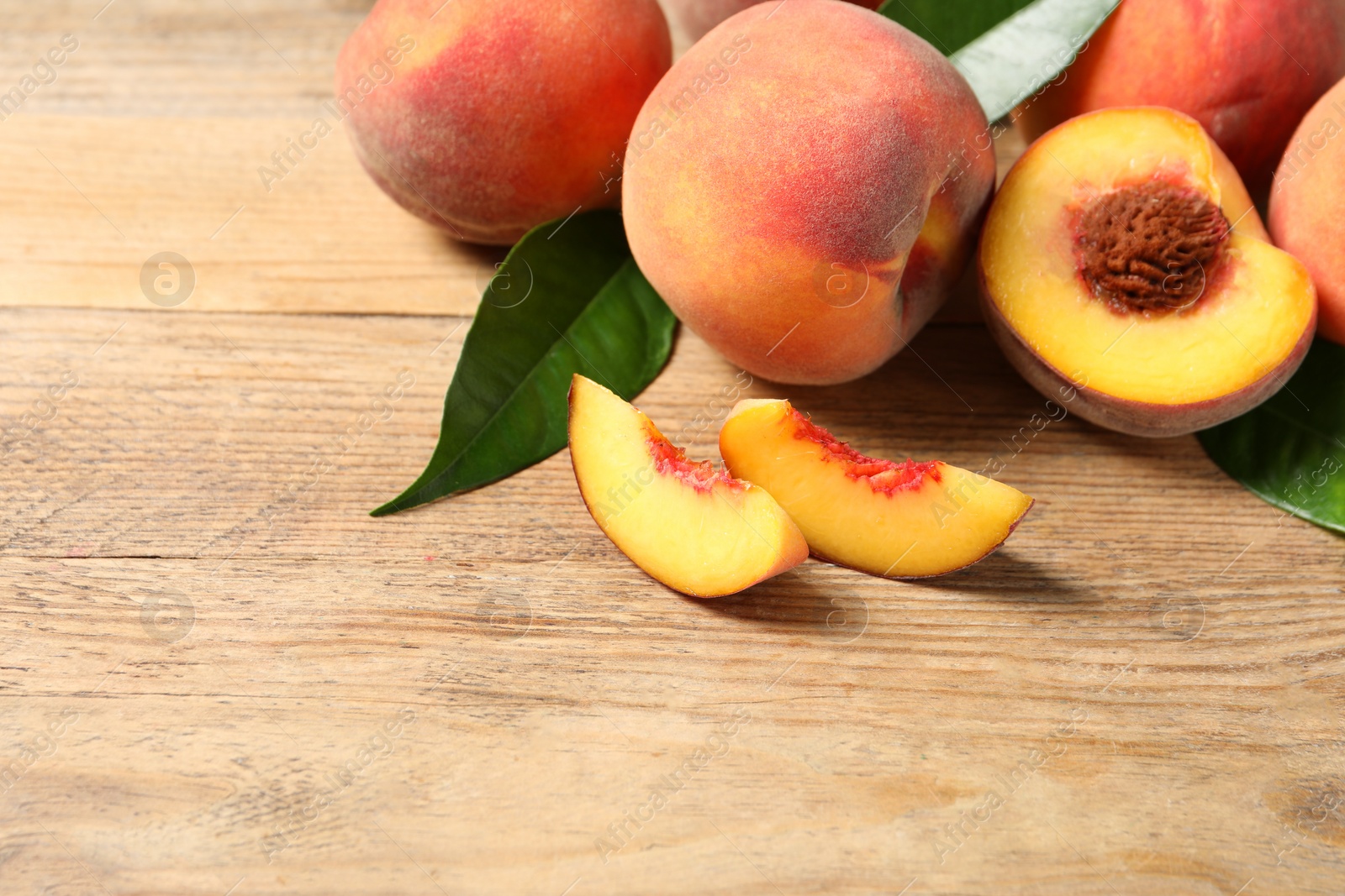 Photo of Cut and whole fresh ripe peaches with green leaves on wooden table, space for text