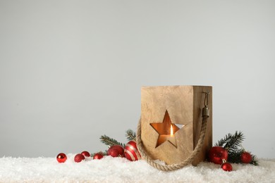 Composition with wooden Christmas lantern on snow against light grey background, space for text