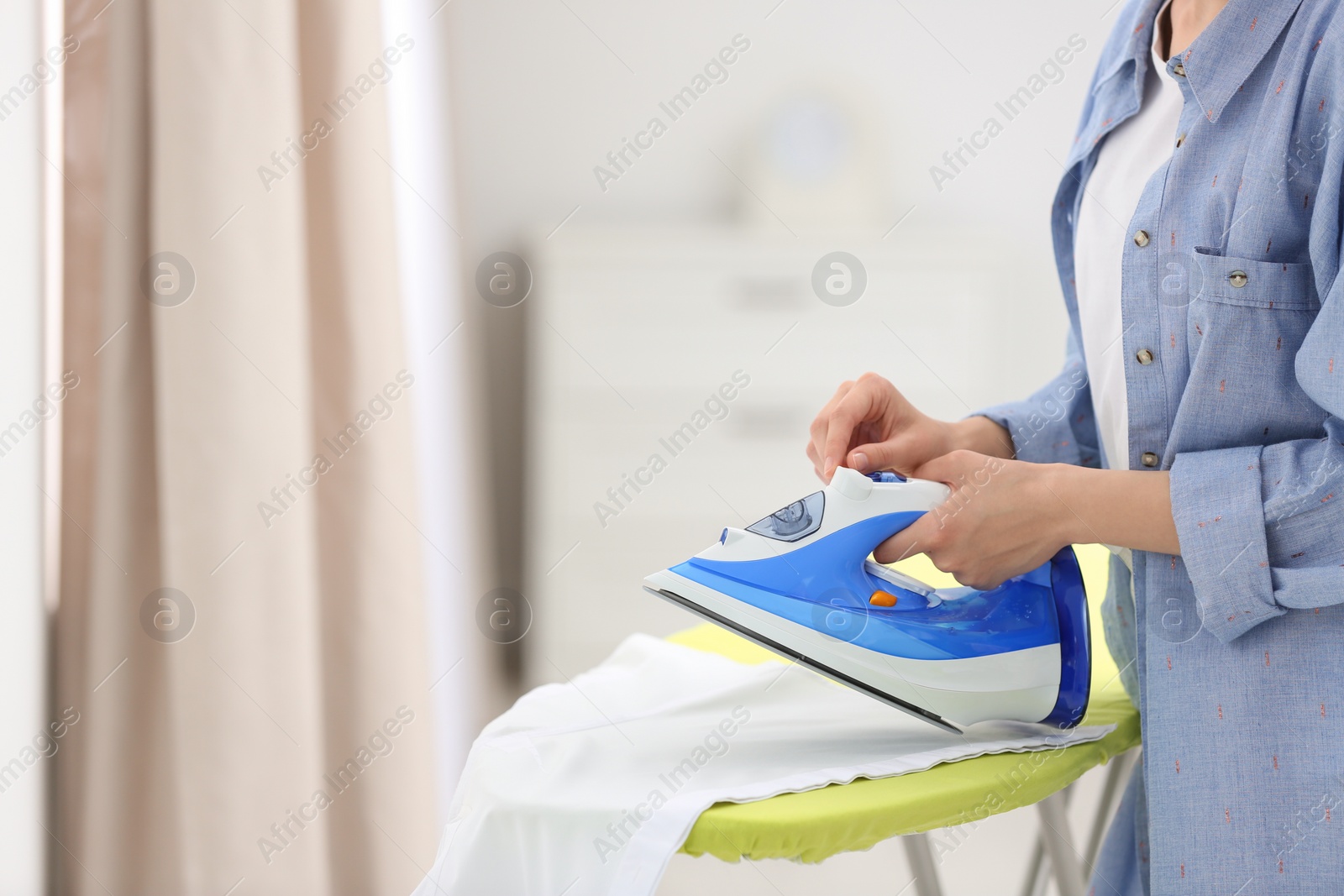 Photo of Young woman ironing clean laundry on board indoors, closeup. Space for text