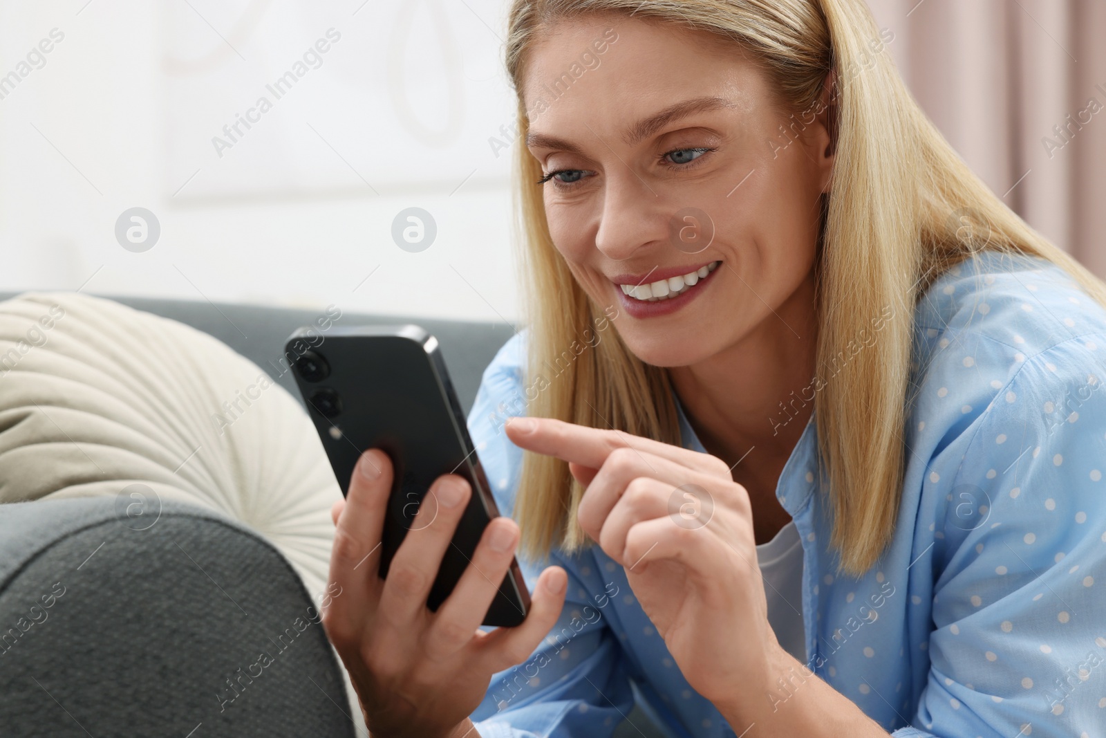 Photo of Happy woman sending message via smartphone on couch at home