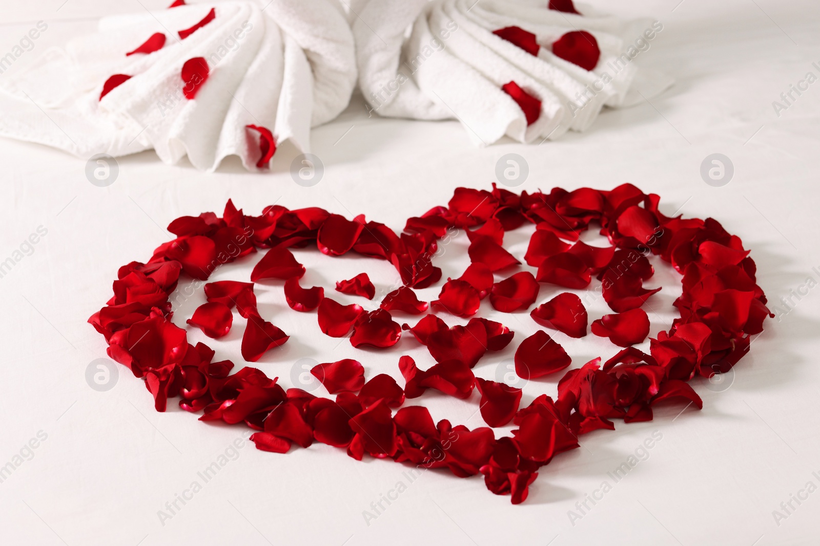 Photo of Honeymoon. Heart made with rose petals on bed, closeup