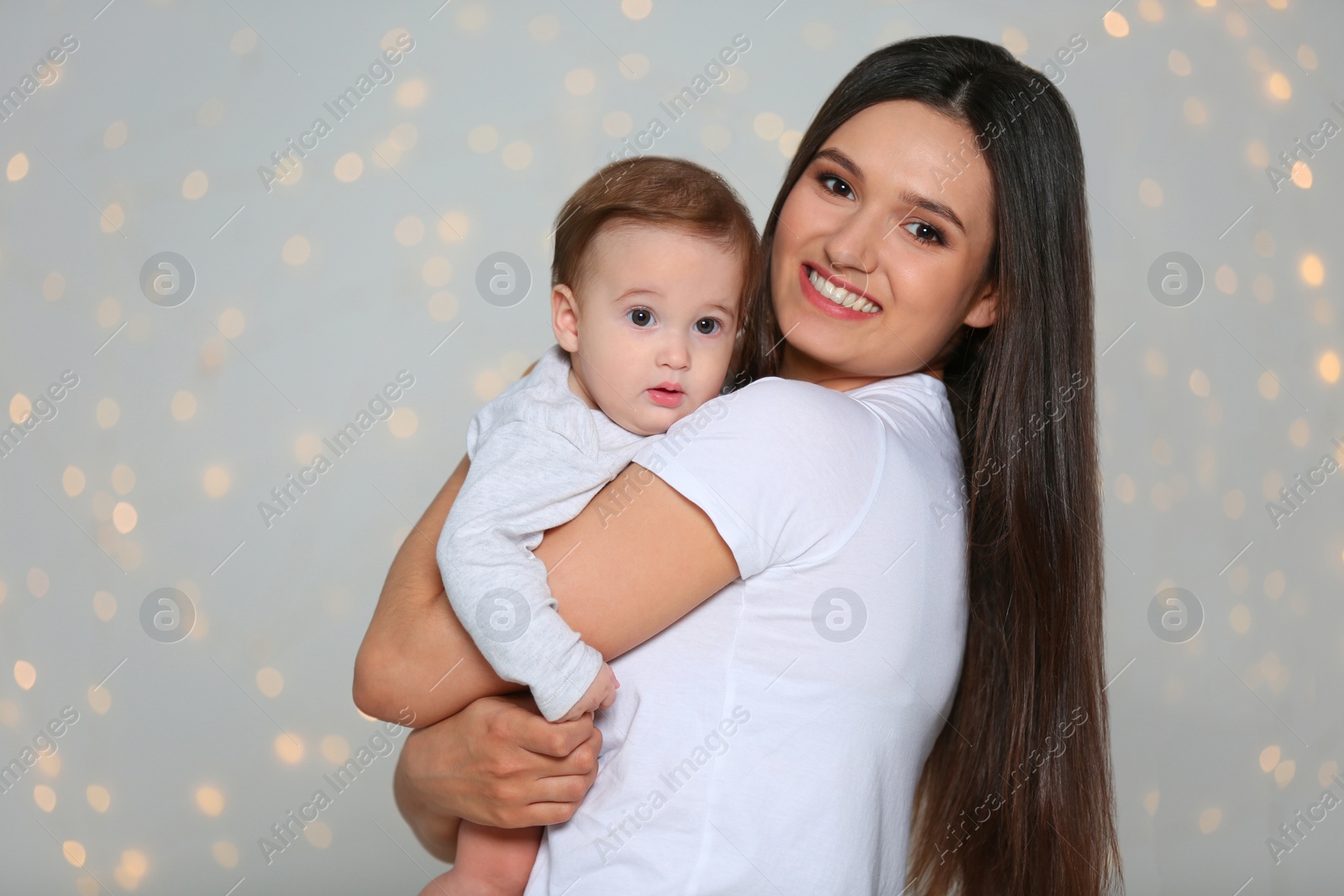 Photo of Portrait of young mother and her adorable baby against defocused lights