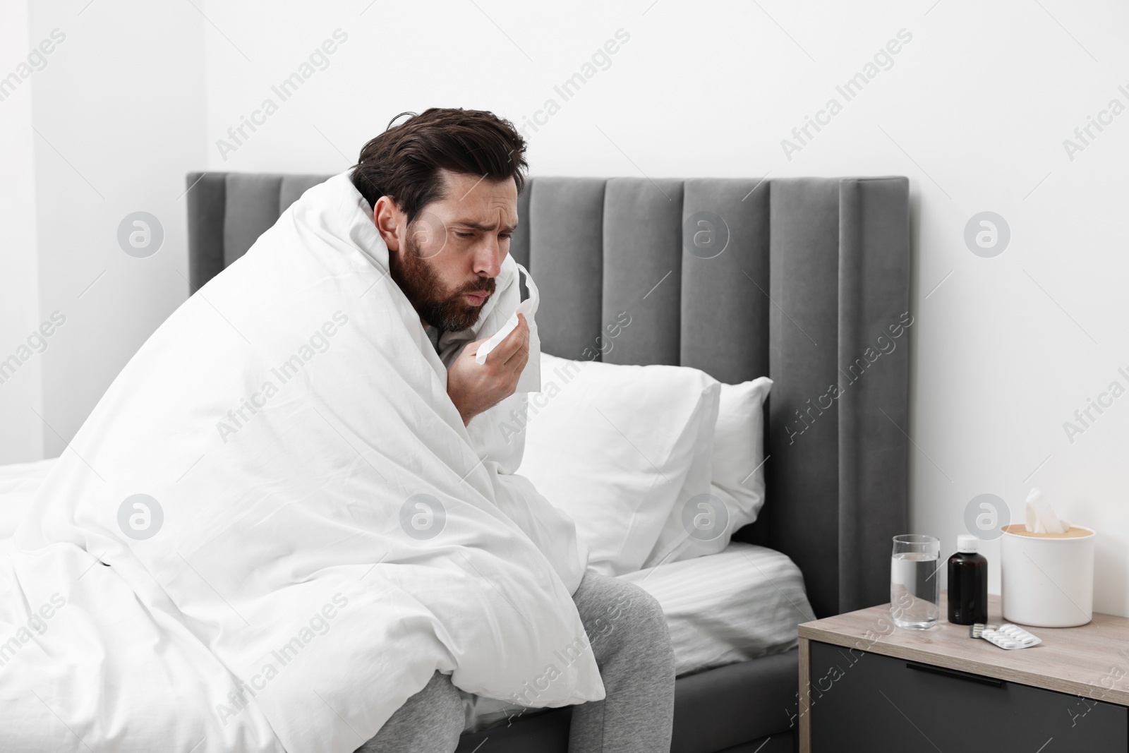 Photo of Sick man with tissue coughing on bed at home. Cold symptoms