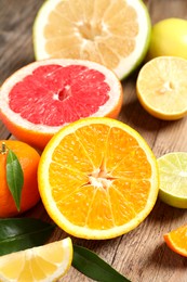 Different ripe citrus fruits with green leaves on wooden table, closeup