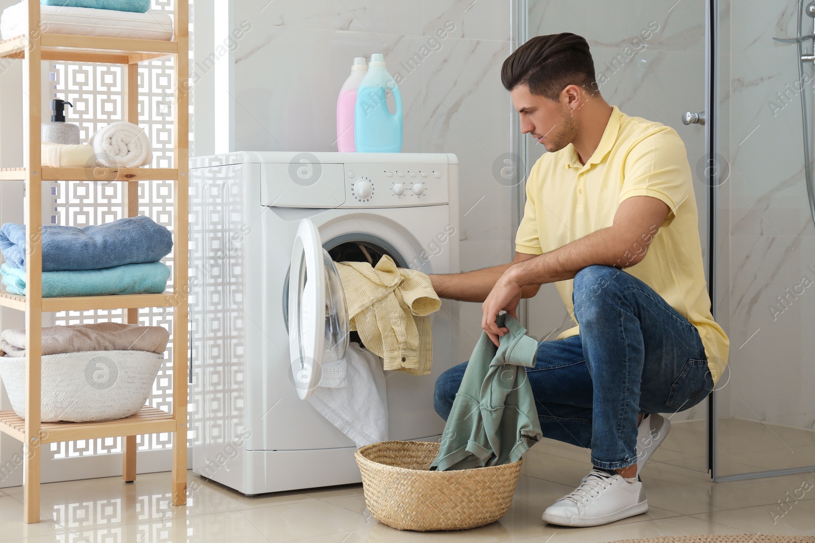 Photo of Man putting clothes into washing machine in bathroom. Laundry day