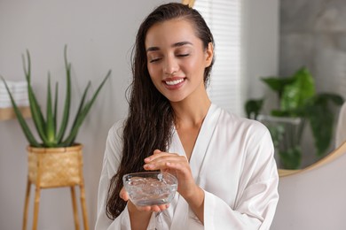 Photo of Young woman holding bowl of aloe hair mask in bathroom