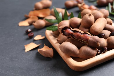 Photo of Wooden plate with delicious ripe tamarinds on black table. Space for text