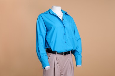 Photo of Female mannequin dressed in leather pants and stylish light blue shirt with necklace on beige background