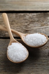 Photo of Organic salt in spoons on wooden table, closeup