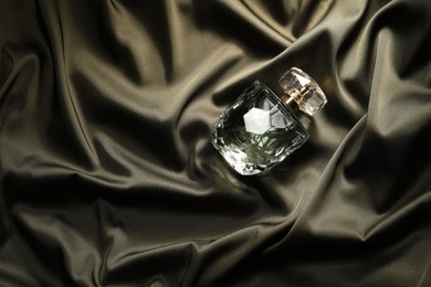 Luxury perfume in bottle on dark silk fabric, top view