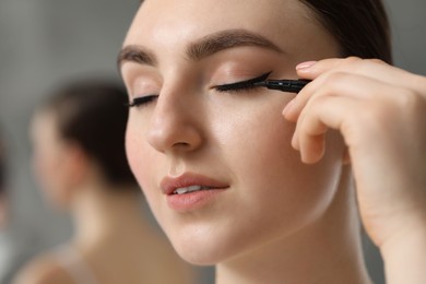 Photo of Makeup product. Woman applying black eyeliner on blurred background, closeup