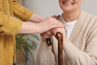 Photo of Caregiver and senior woman with walking cane sitting at home, closeup