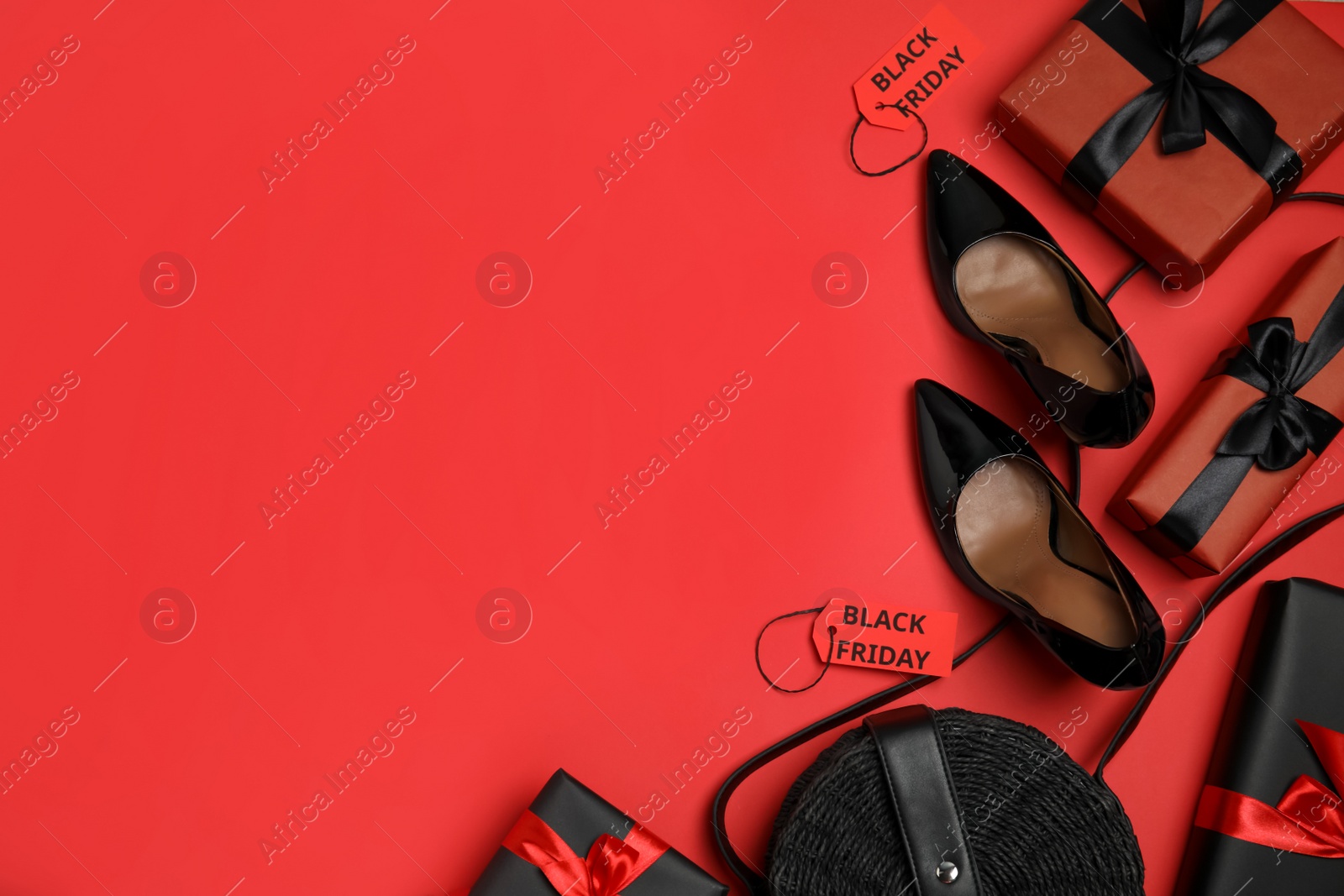 Photo of Gift boxes, women's accessories, shoes and space for text on red background, flat lay. Black Friday sale