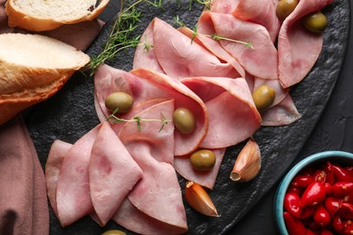 Photo of Tasty ham with olives, garlic, bread and pickled peppers on black table, flat lay