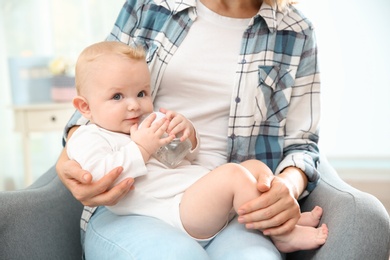 Photo of Lovely mother giving her baby drink from bottle in room