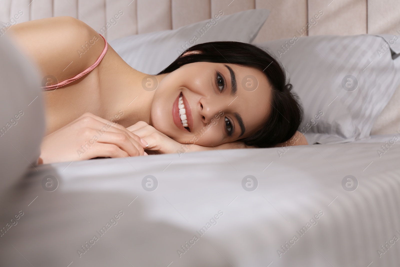 Photo of Woman lying in comfortable bed with light grey striped linens