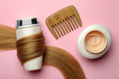 Photo of Bottle wrapped in lock of hair, jar and comb on pink background, flat lay. Natural cosmetic products