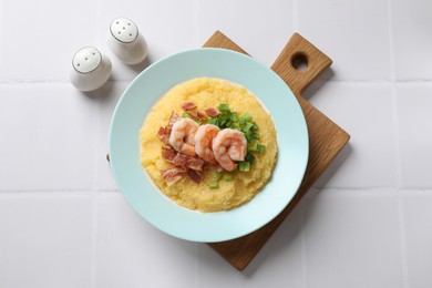 Plate with fresh tasty shrimps, bacon, grits and green onion on white tiled table, top view