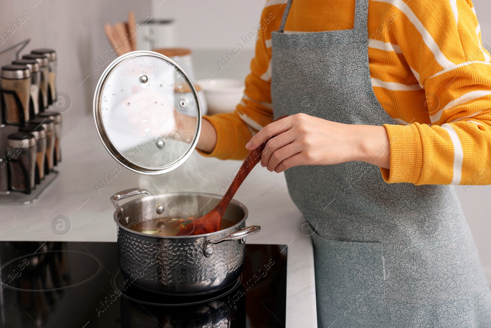 Photo of Woman cooking soup on cooktop in kitchen, closeup