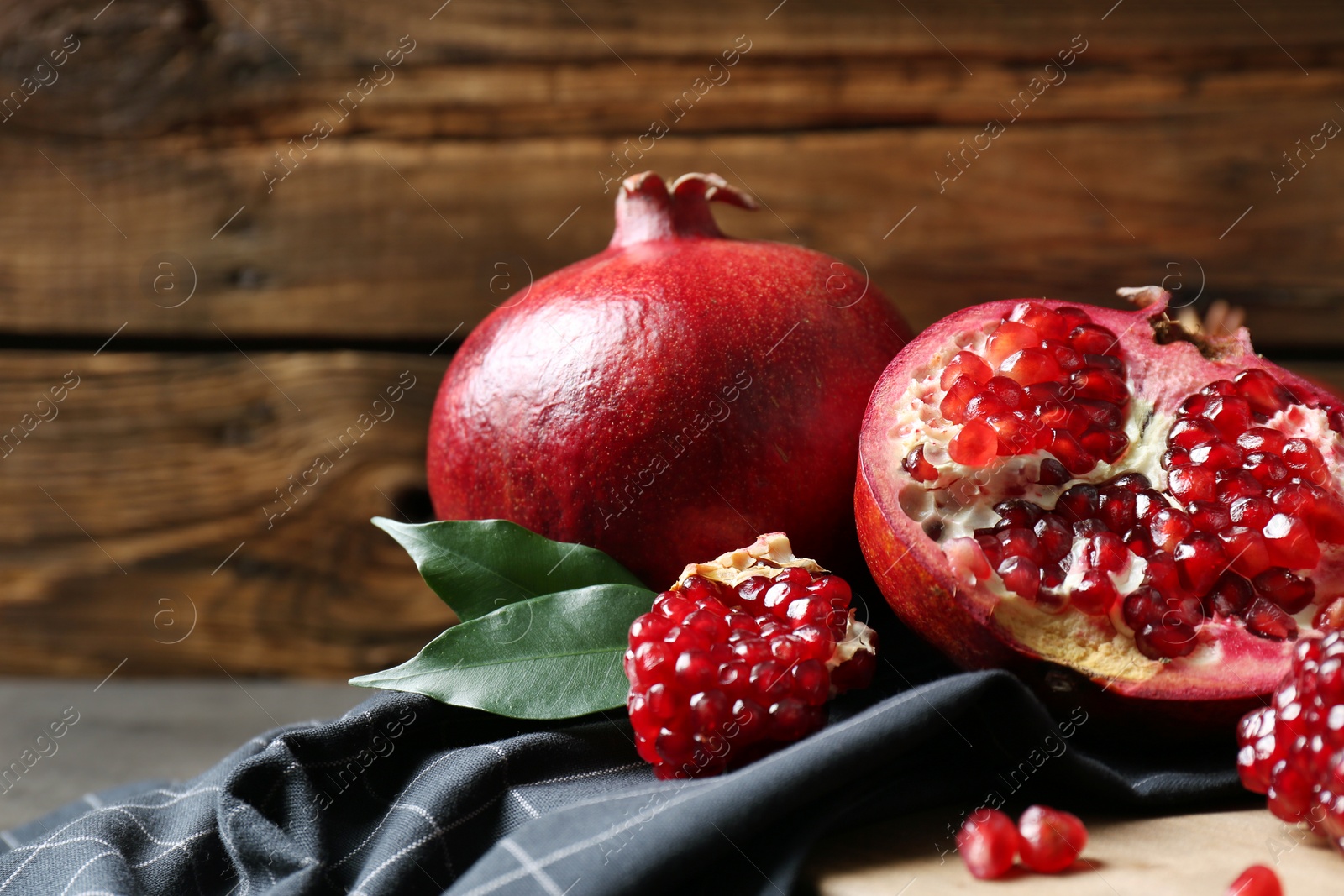 Photo of Ripe pomegranates on board against wooden background, space for text