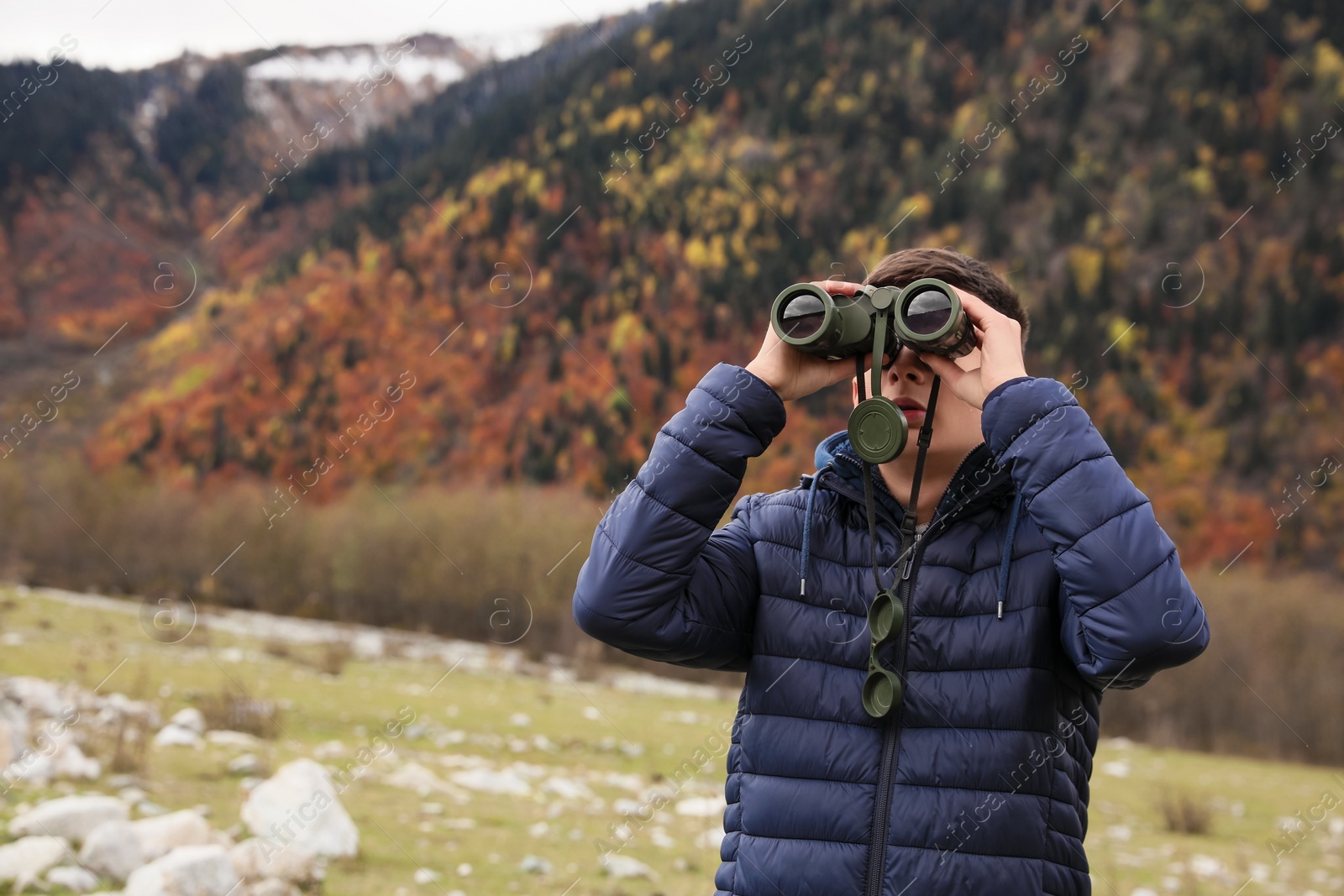 Photo of Boy looking through binoculars in beautiful mountains. Space for text