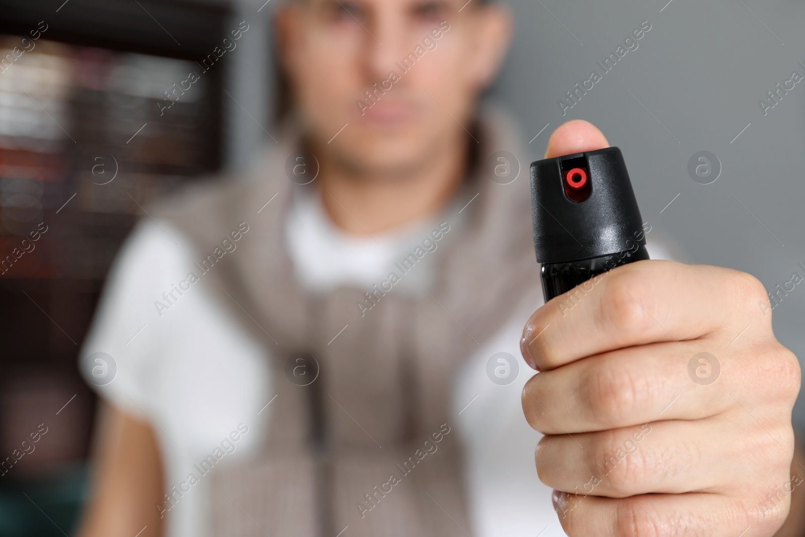 Photo of Man using pepper spray indoors, focus on hand. Space for text