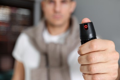 Man using pepper spray indoors, focus on hand. Space for text