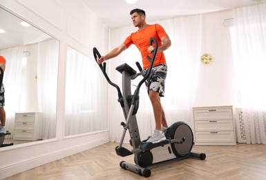 Photo of Man using modern elliptical machine at home