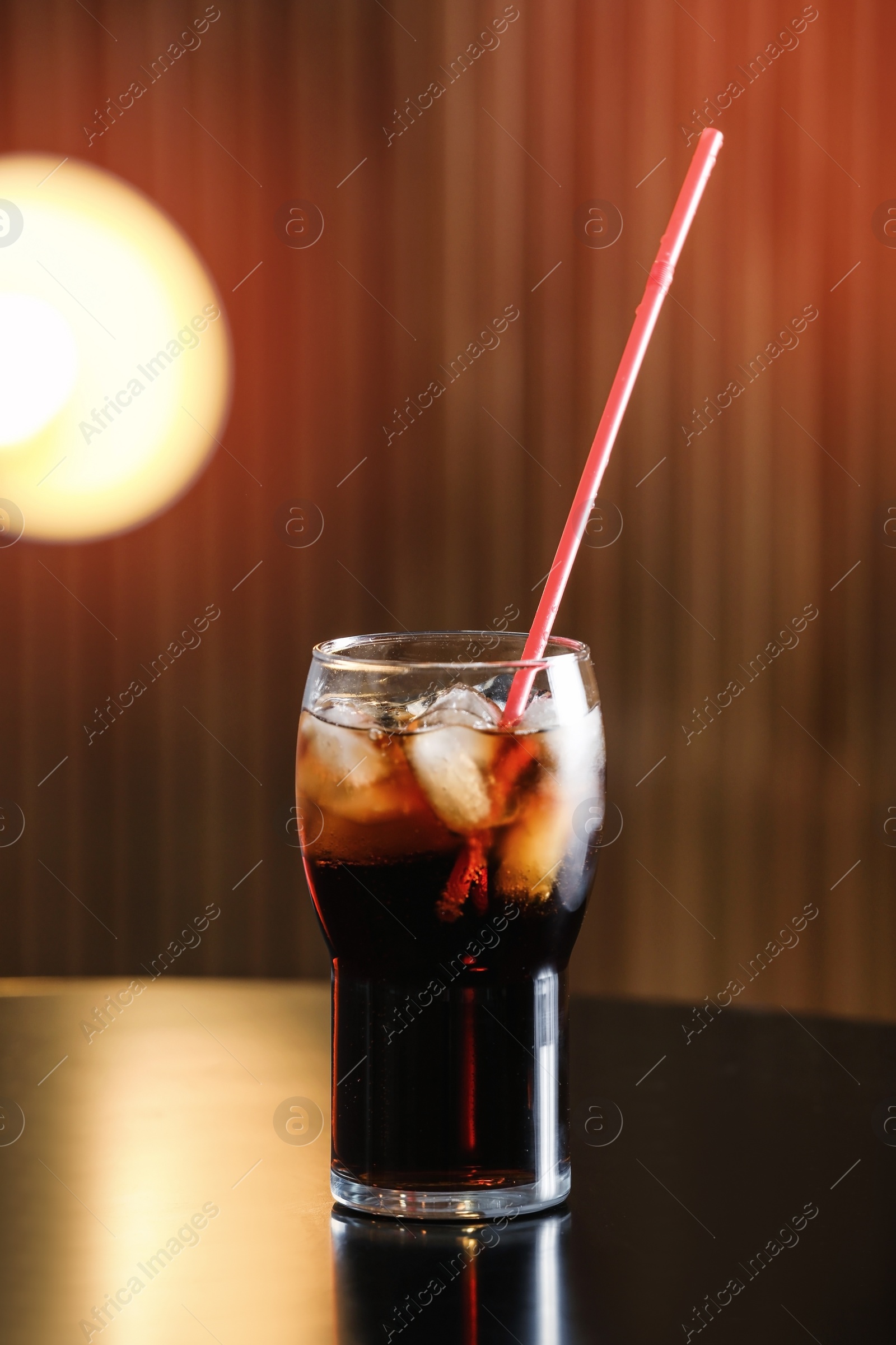 Photo of Glass of cola with ice on table against blurred background