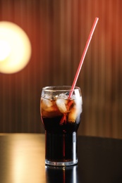 Glass of cola with ice on table against blurred background