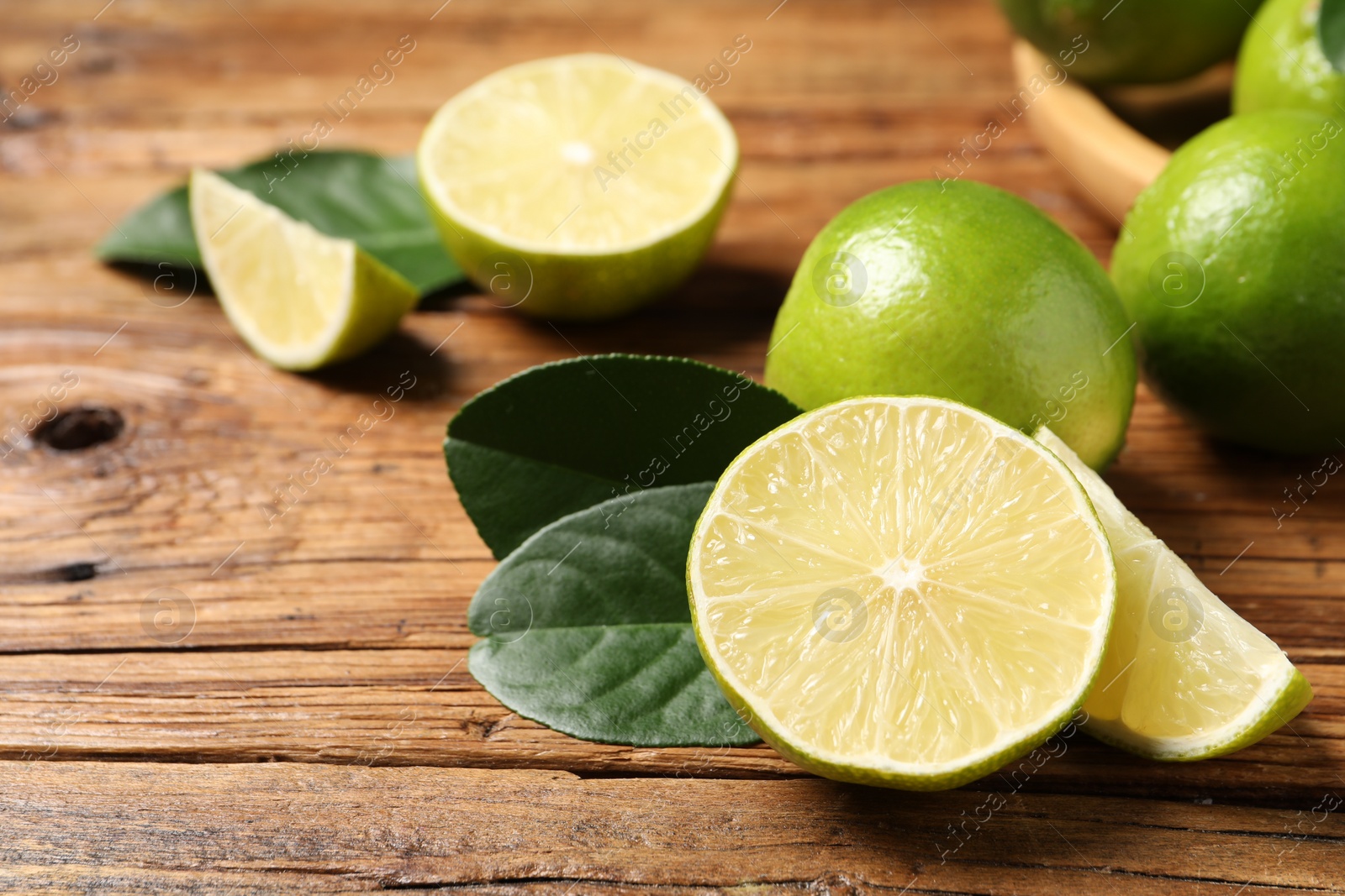 Photo of Fresh ripe limes and green leaves on wooden table, closeup. Space for text