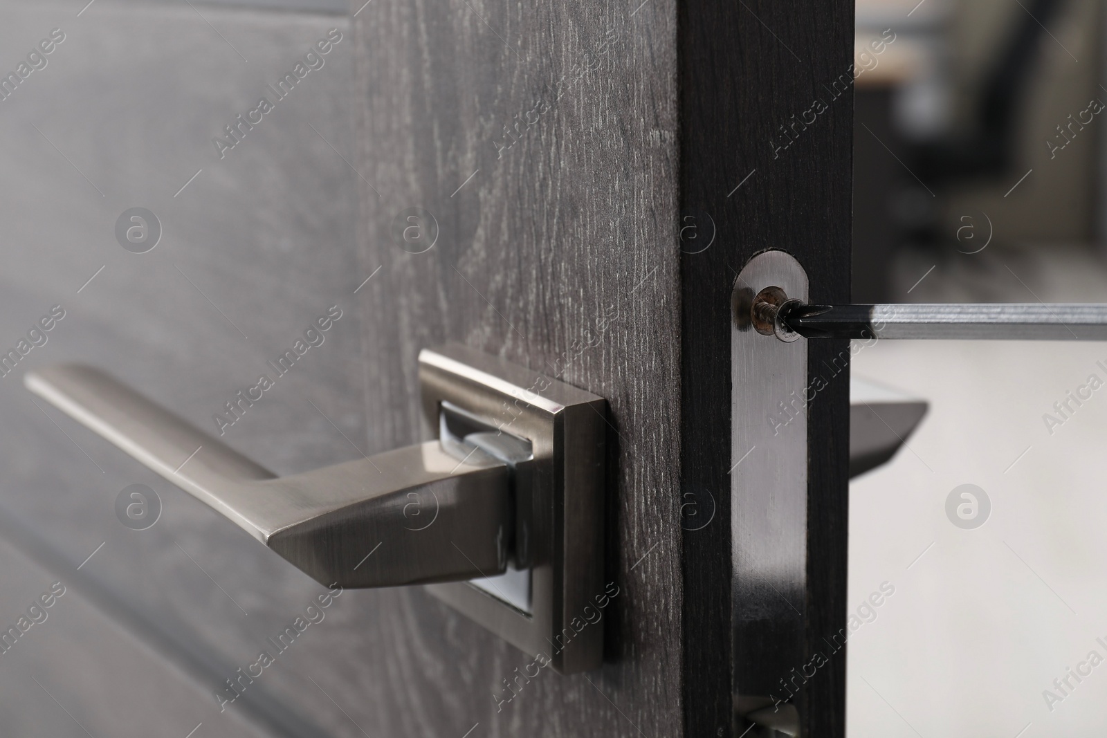 Photo of Repairing door handle with screwdriver indoors, closeup