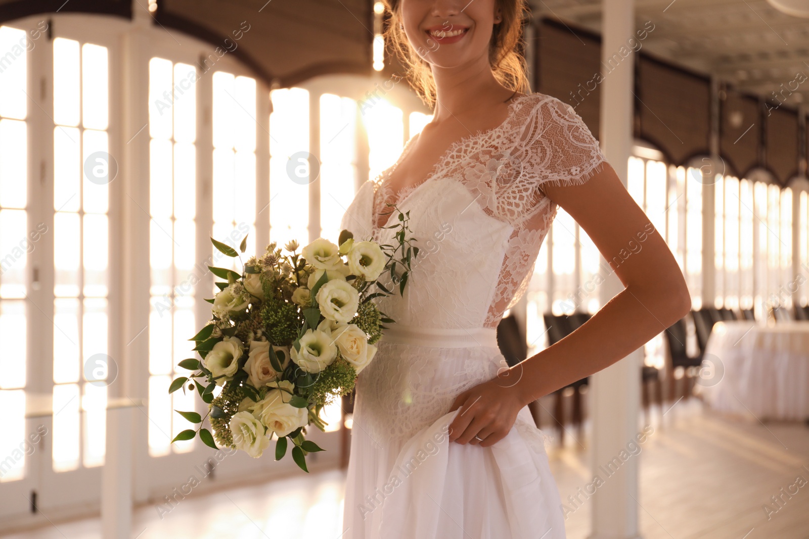 Photo of Bride in beautiful wedding dress with bouquet in restaurant, closeup