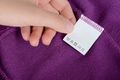 Woman holding white clothing label on purple garment, closeup