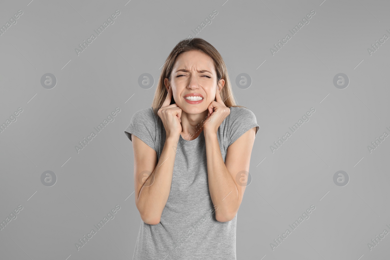 Photo of Emotional young woman covering her ears with fingers on grey background
