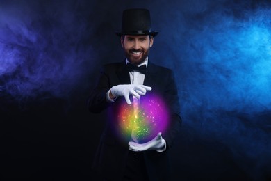 Image of Magic and sorcery. Magician with fantastic light in smoke on dark background