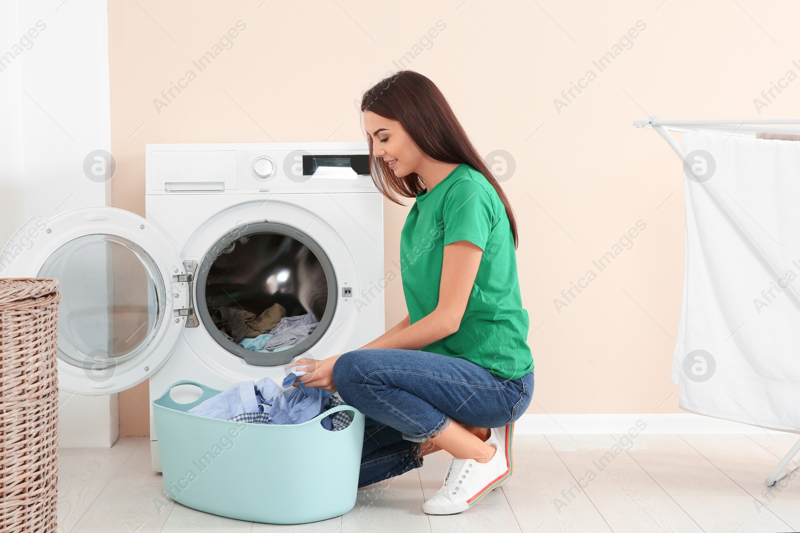 Photo of Young woman taking laundry out of washing machine at home