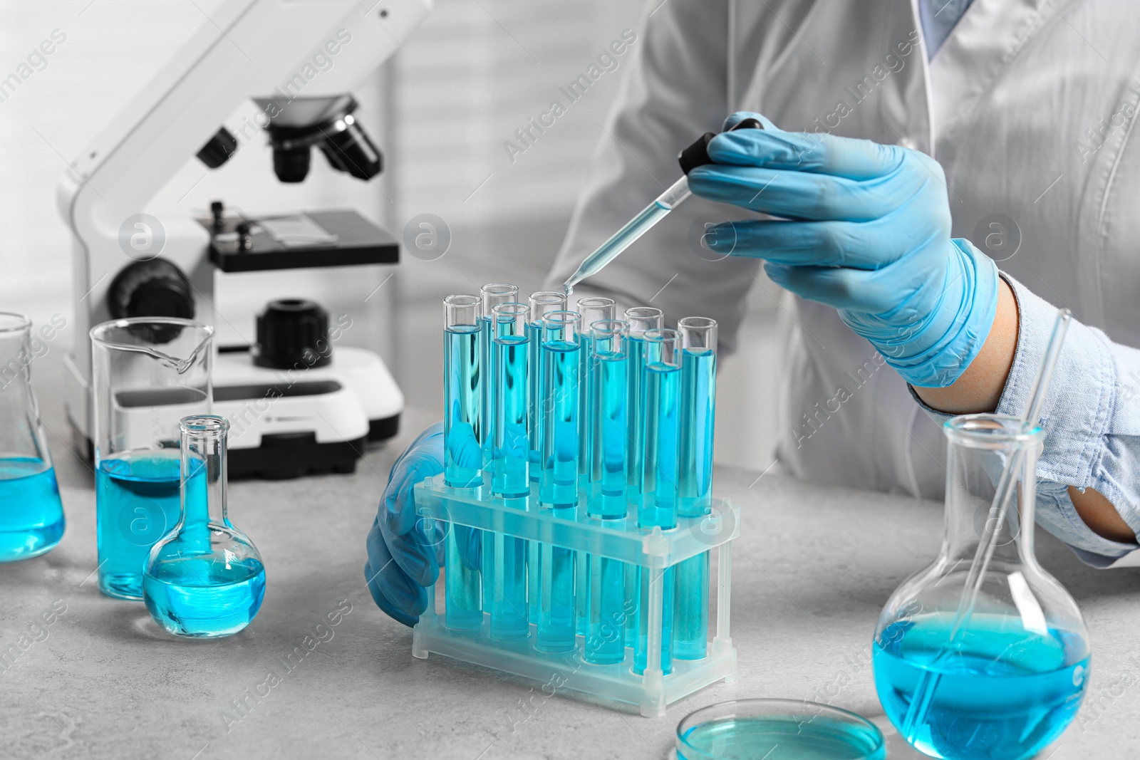 Photo of Scientist dripping liquid from pipette into test tube at white table in laboratory, closeup