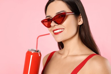 Photo of Beautiful young woman with stylish sunglasses drinking from tin can on pink background