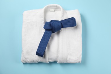 Photo of Karate belt and white kimono on light blue background, top view