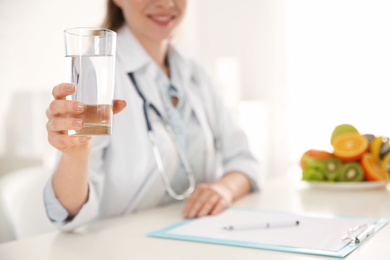 Photo of Nutritionist with glass of water at desk in office, closeup. Space for text