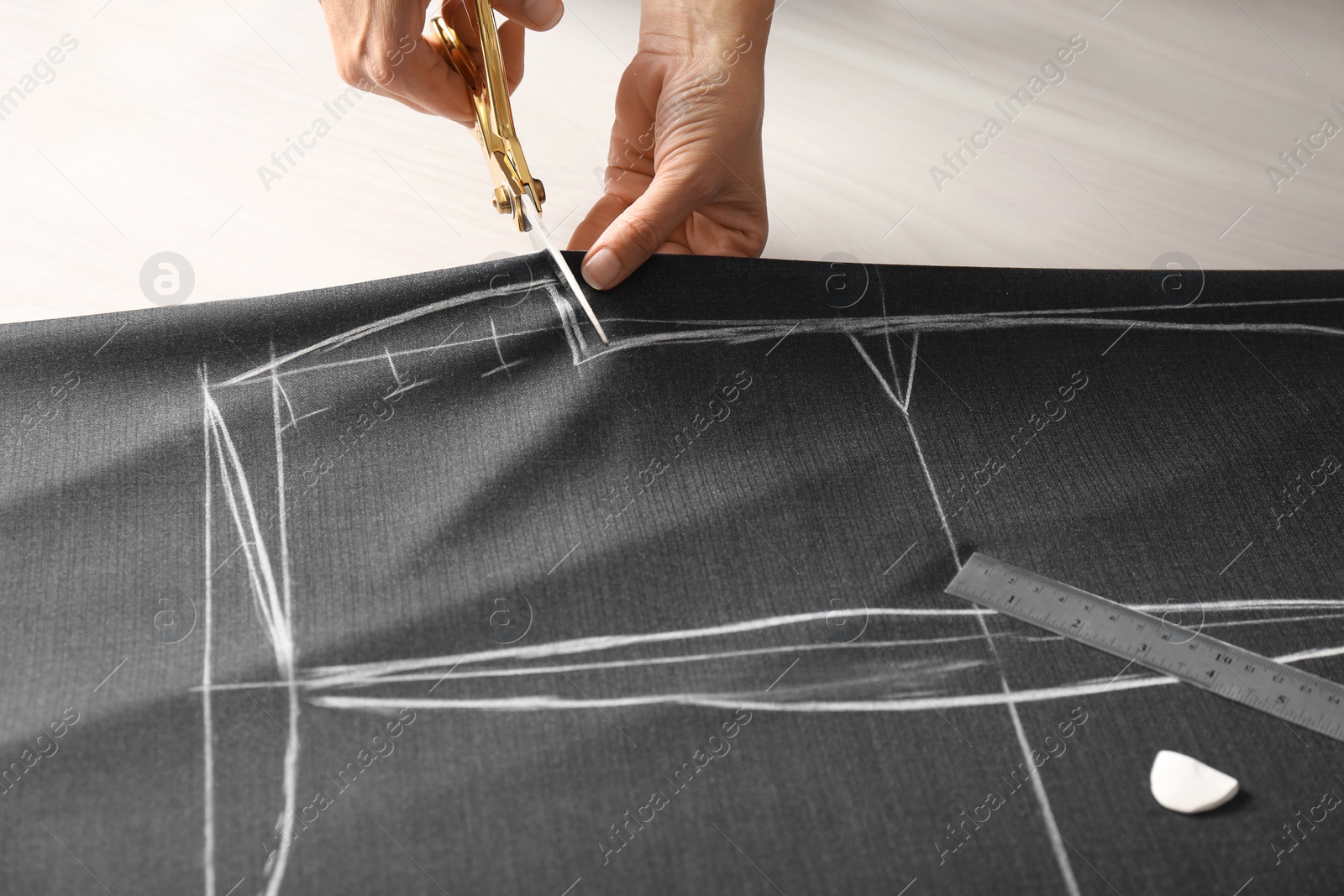 Photo of Seamstress cutting fabric following chalked sewing pattern at table in workshop, closeup