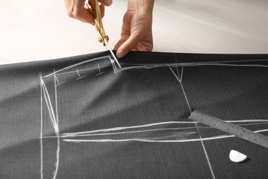 Seamstress cutting fabric following chalked sewing pattern at table in workshop, closeup