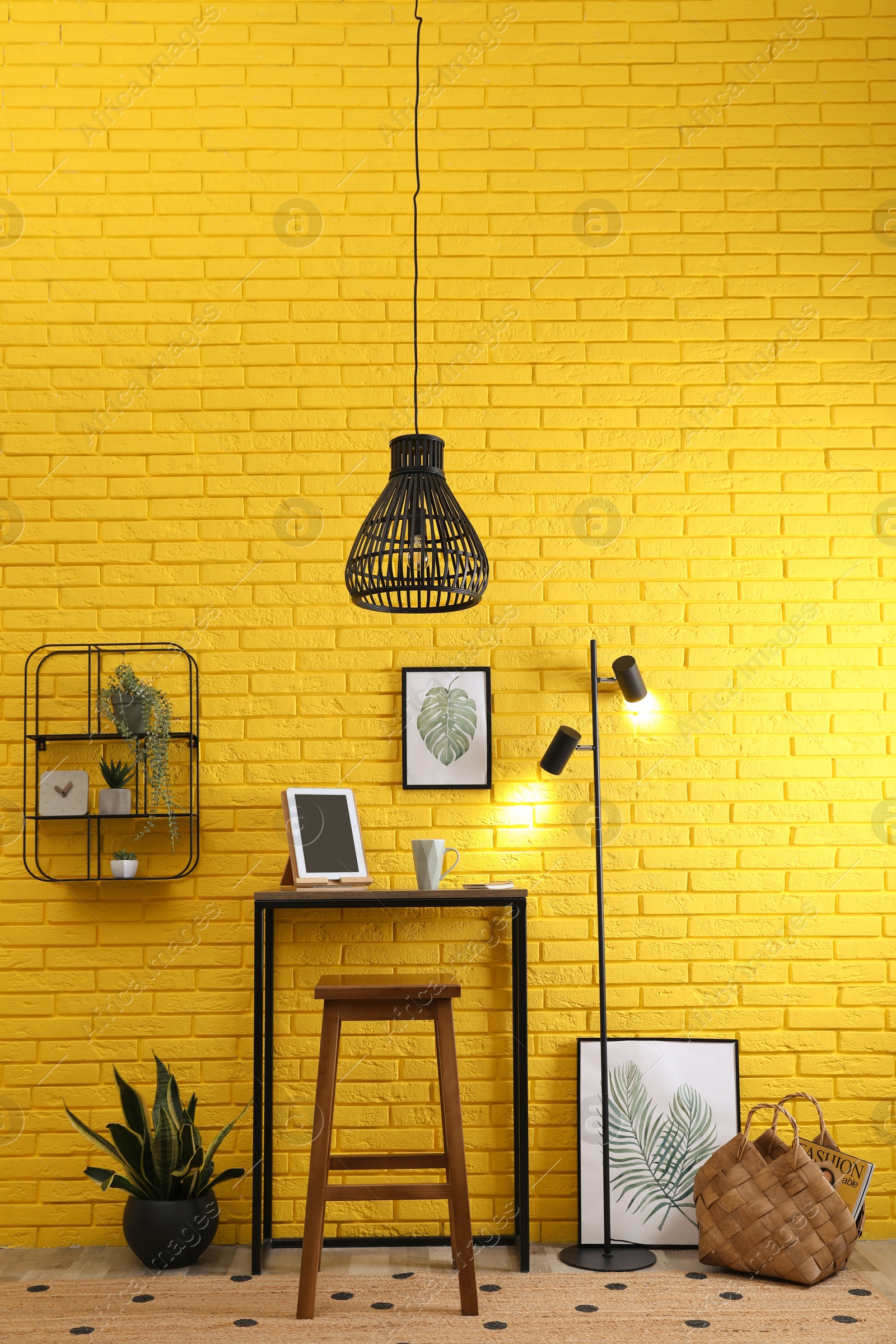 Photo of High wooden table with tablet and stool as stand up workplace near yellow brick wall. Stylish interior